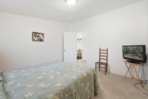 A bedroom with a bed, a television on a stand, a chair, and a door leading to another room. - Fisherman's Rest - Handicap Accessible! (Taylor County)