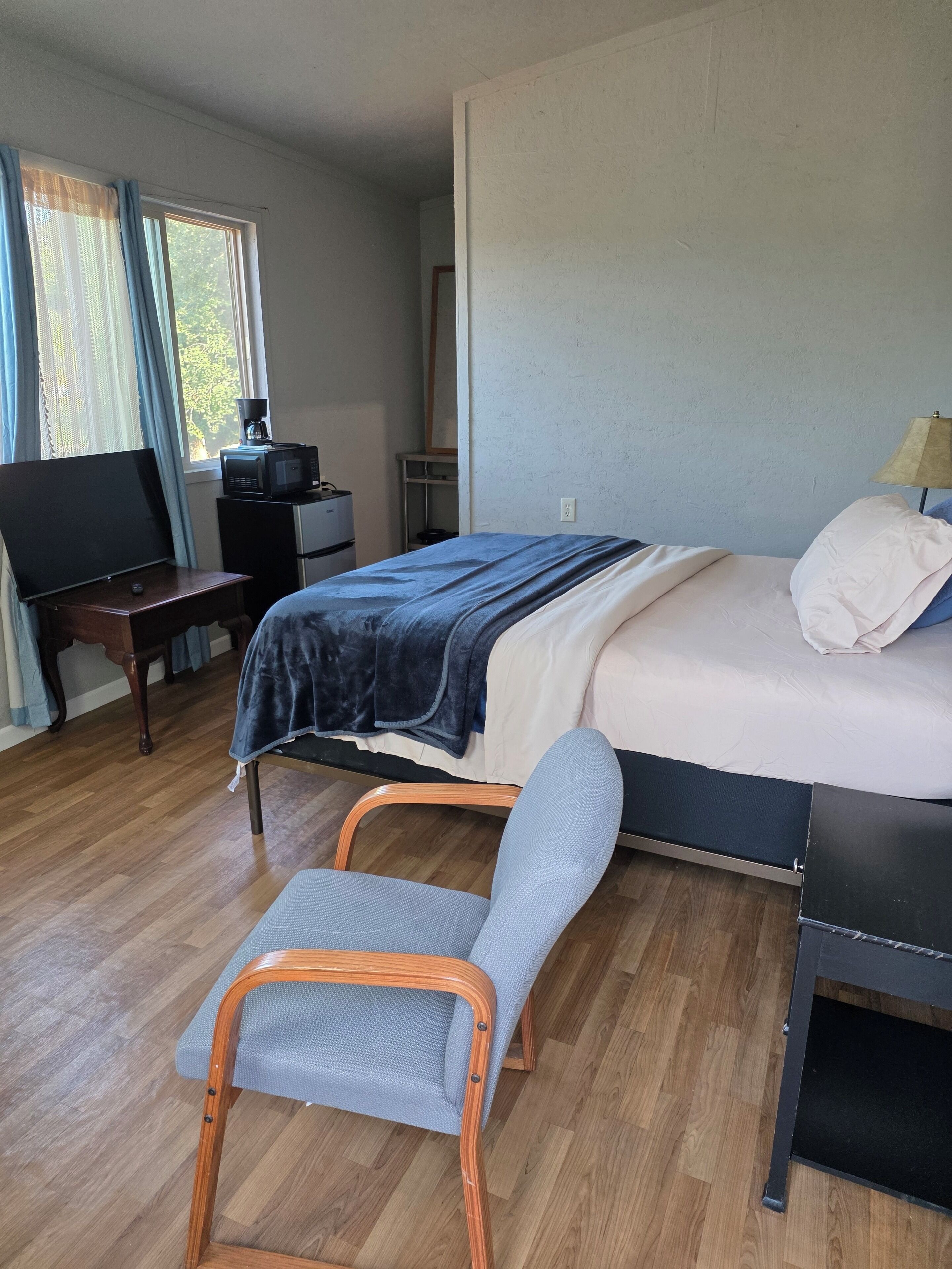 A bedroom with a bed, bedside table, chair, and a desk with a television.