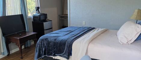 A bedroom with a bed, bedside table, chair, and a desk with a television.