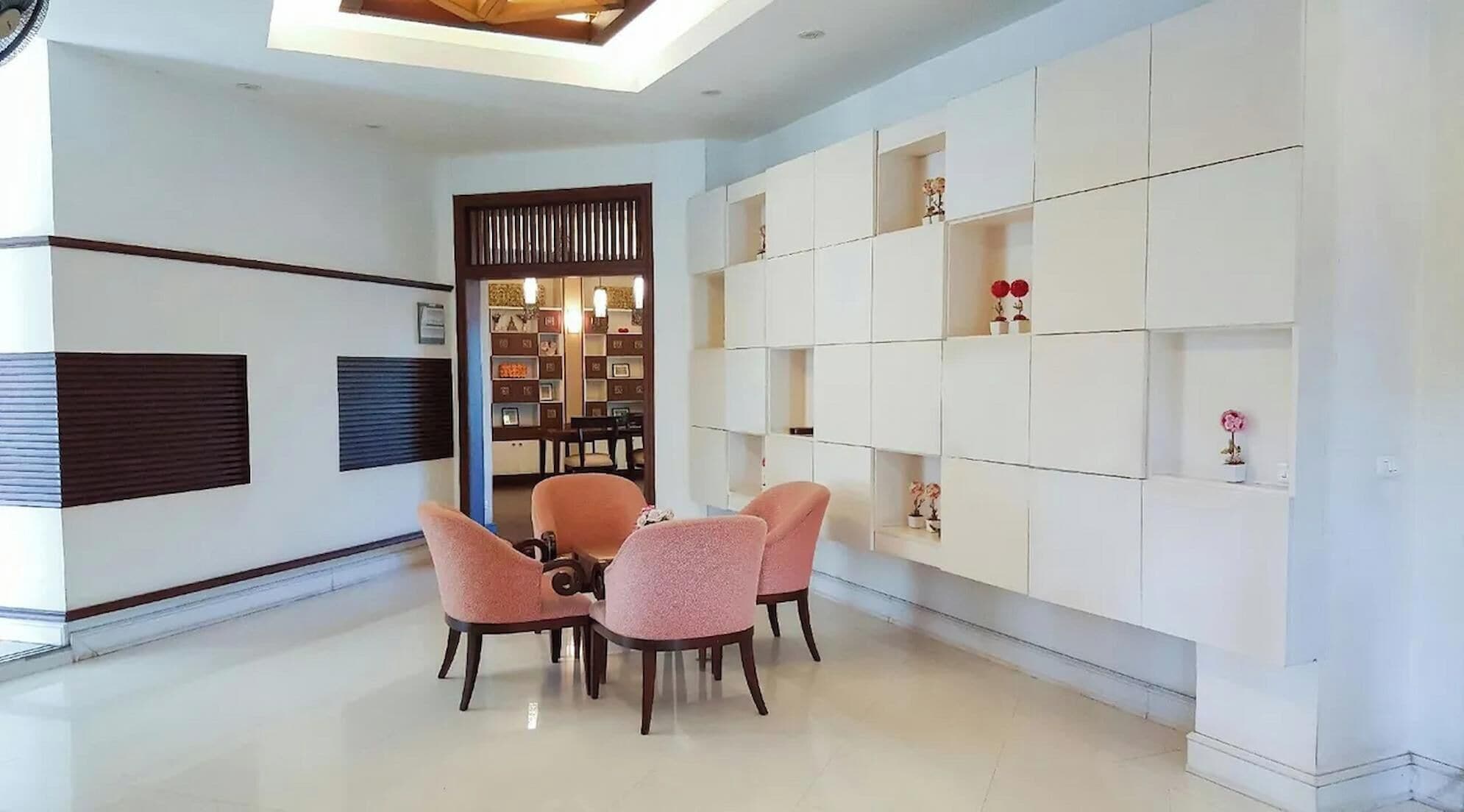 Un área de comedor moderna con suelo de baldosas blancas, una mesa de comedor con cuatro sillas y un estante blanco con objetos decorativos.