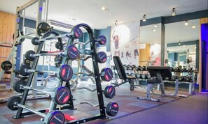 Un gimnasio con equipo de levantamiento de pesas, incluyendo una jaula de sentadillas y mancuernas.