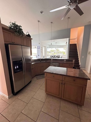 Una cocina moderna con refrigerador empotrado, armarios de madera, encimera de granito y ventilador de techo.