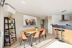 A modern kitchen with a wooden dining table, bar stools, and a painting above the table. - Location Plus Nelson family getaway (Nelson)