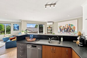 A modern kitchen with a dishwasher, a sink, and a countertop. There are windows with a view of the outdoors, and a painting on the wall.