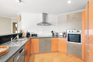A modern kitchen with stainless steel appliances, wooden cabinets, and a black countertop. - Location Plus Nelson family getaway (Nelson)