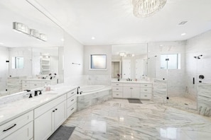 Une salle de bain moderne dotée d’un grand meuble-lavabo en marbre, d’une baignoire sur pieds et d’une douche séparée par des parois en verre.
