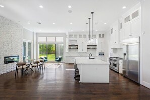 A modern kitchen with a large island, white cabinetry, and a dining area with a view of the outdoors. - Houston’s Private Estate Venue | Weddings & Events (Houston)