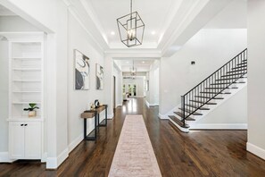 A spacious hallway with a wooden floor, a central light fixture, and a staircase on the right. - Houston’s Private Estate Venue | Weddings & Events (Houston)