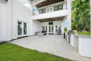 A two-story house with a covered patio area, a seating arrangement, and a grill station. - Houston’s Private Estate Venue | Weddings & Events (Houston)