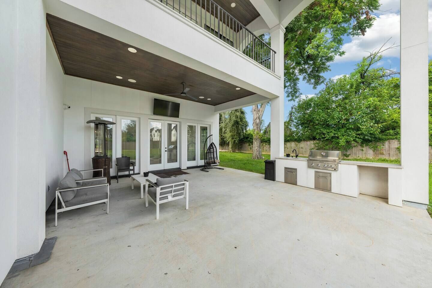 A covered outdoor patio with a grill, seating area, and a view of the backyard.