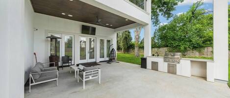 A covered outdoor patio with a grill, seating area, and a view of the backyard.