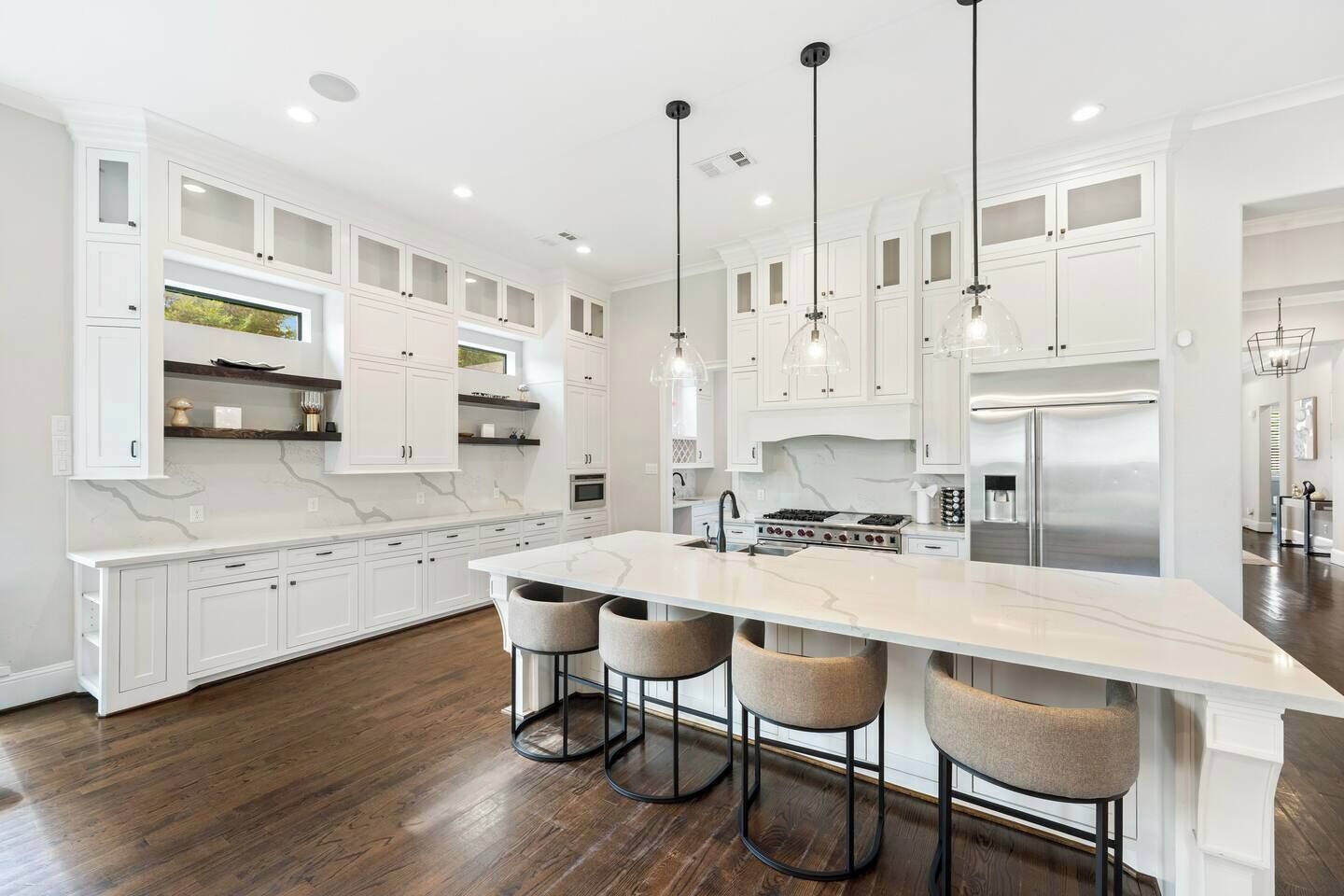 Una cocina moderna con gabinetes blancos, una isla grande con taburetes de bar y electrodomésticos de acero inoxidable.