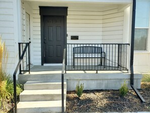 A house with a black front door, a concrete porch with a metal railing, and a small bench. - Delightful Home with W&D and Office in Salt Lake City (Salt Lake City)