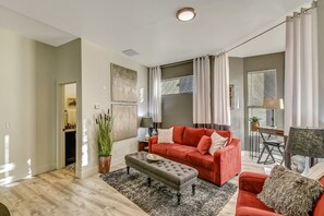 A living room with a red sofa, a grey ottoman, and a dining area with a table and chairs. - Delightful Home with W&D and Office in Salt Lake City (Salt Lake City)