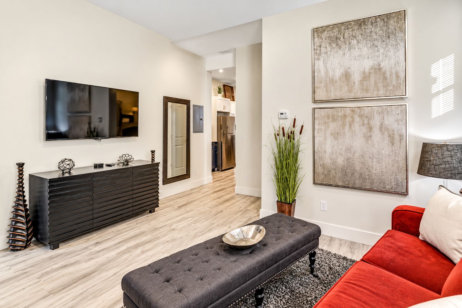 A modern living room with a dark-colored sofa, a red accent piece, a black entertainment unit, and artwork on the walls.