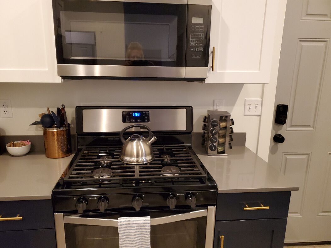 A kitchen with a stove, microwave, oven, and a kettle.
