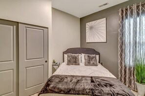 A bedroom with a bed, a nightstand, a wall art piece, and a window with curtains. - Delightful Home with W&D and Office in Salt Lake City (Salt Lake City)