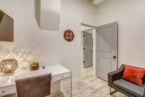Une pièce moderne avec un bureau blanc, une chaise marron, un canapé gris agrémenté d’un coussin orange et un élément décoratif mural.
