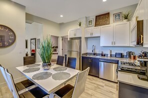 A modern kitchen with white cabinets, stainless steel appliances, and a dining area with a table set for four. - Delightful Home with W&D and Office in Salt Lake City (Salt Lake City)