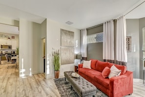 A modern living room with a red sofa, a grey ottoman, and a large potted plant.