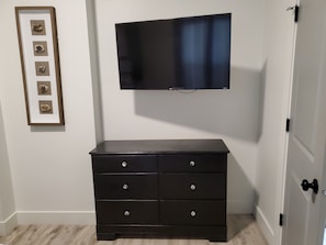 A room with a black dresser, a framed picture on the wall, and a mounted flat-screen TV.