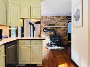 A kitchen with light green cabinets, a stone wall, and a wood-burning stove. - Private 7-Acre Retreat w/Brook, Near Hike & Ski (Townshend)
