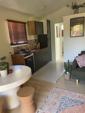 Una cocina compacta con electrodomésticos modernos, un comedor con mesa redonda y una sala de estar con sofá y una planta de cactus.