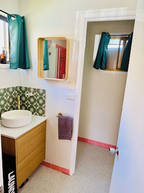 Un baño con un lavamanos redondo, un espejo, un perchero y una puerta que da a otra habitación.