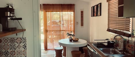 A kitchen with a round table, a coffee machine, and a window with blinds.