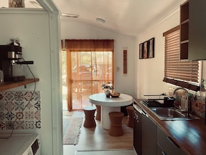 A kitchen with a round table, a coffee machine, and a window with blinds.