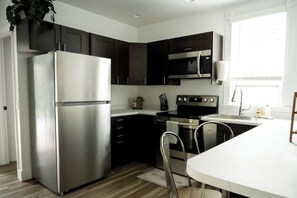 A modern kitchen with stainless steel appliances, dark cabinetry, and a white dining area.