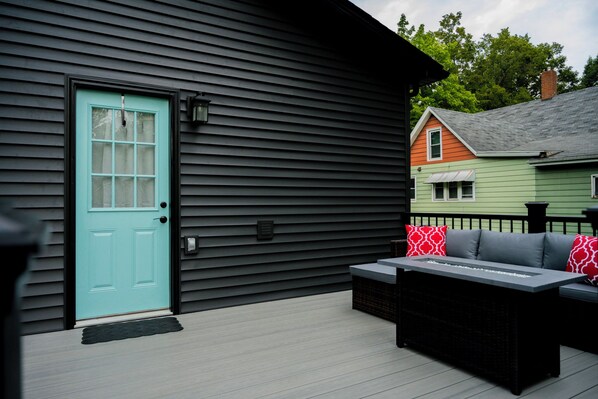 A deck with outdoor seating, a teal door, and a black exterior wall.