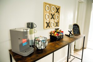 A coffee station with a Keurig machine, a coffee mug, a basket of snacks, and a welcome sign.