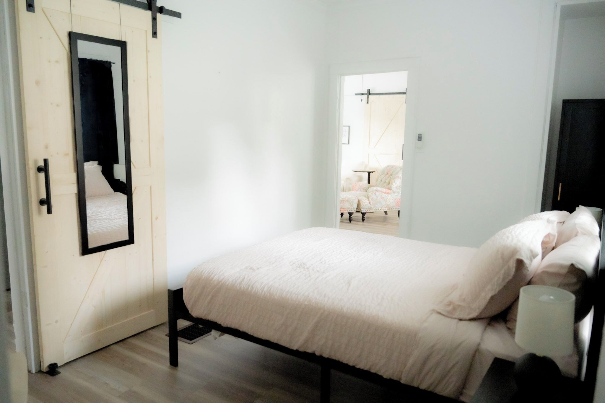Un dormitorio con cama, una puerta con espejo y vistas a otra habitación.