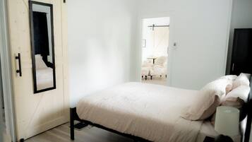 Un dormitorio con cama, una puerta con espejo y vistas a otra habitación.