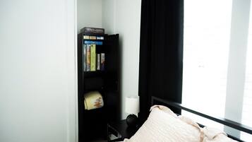 A bedroom with a bed, a bookshelf, a window with curtains, and a bedside table with a lamp.