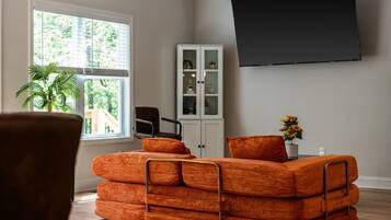 A living room with a sofa, a cabinet, a TV, and a window with blinds.