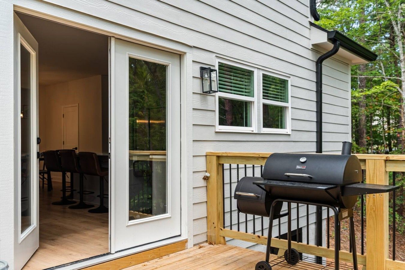 A wooden deck with a barbecue grill, a sliding glass door leading to an interior dining area, and a window with shutters.