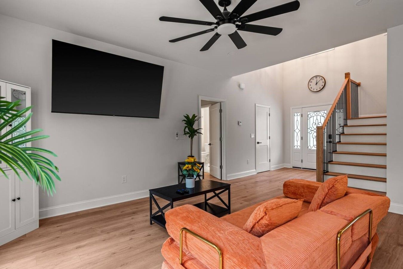 A living room with a ceiling fan, a black coffee table, an orange sofa, and a staircase with a wooden railing.
