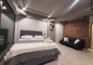 Une chambre à coucher moderne avec un grand lit, un canapé noir et un mur décoratif en briques.