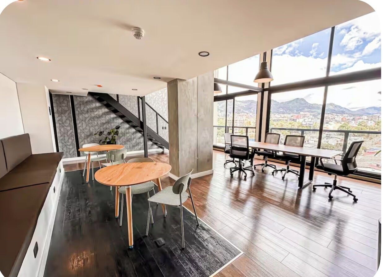 A modern conference room with a large table and chairs, a staircase, and a view of mountains through large windows.
