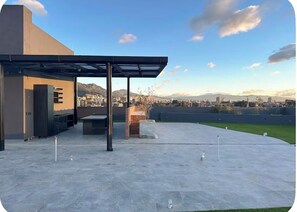 An outdoor patio area with a covered seating area, a flat roof, and a view of a cityscape and mountains in the distance. - Modern & Cozy Apartment in North Bogotá (Bogotá)