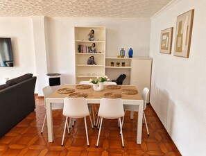 Una sala de estar moderna con una mesa de comedor, sillas blancas, un sofá y una estantería.