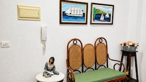 Una habitación con piso de madera, un banco acolchado verde, una pequeña mesa con una figurita y dos cuadros en la pared.