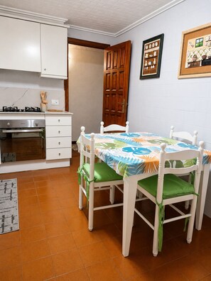 A compact kitchen with white cabinets, a stove, and an oven. A dining table with chairs is positioned in front of the kitchen.