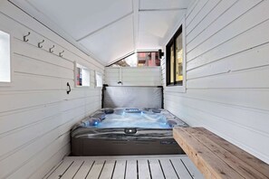 Ein Whirlpool in einem schmalen Raum mit weißen Wänden, einer Holzbank und einem Fenster.