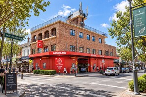 A brick building with a red Liquorland sign, a pedestrian crossing, and a street sign for Marrickville Rd. - Cozy Room | Private Shower, Heart of Marrickville (Marrickville)