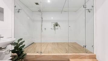 A modern bathroom with a glass-enclosed shower, a sink, and a potted plant.