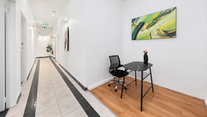 A hallway with a tiled floor, a black office chair, a small table, and a painting on the wall.