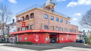 A red-brick building with a flat roof and a balcony on the second floor.